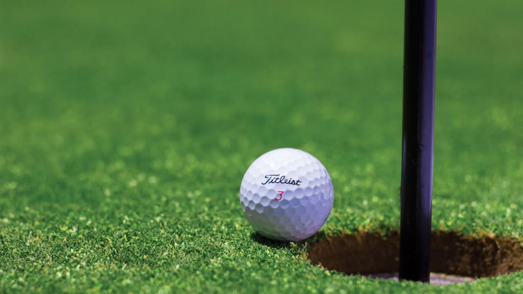 Close-up of a Titleist golf ball next to a golf hole on a green course.